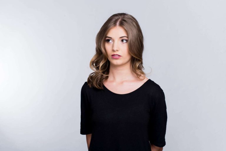 Nachdenkliche Frau in schwarzem Oberteil vor neutralem Hintergrund.